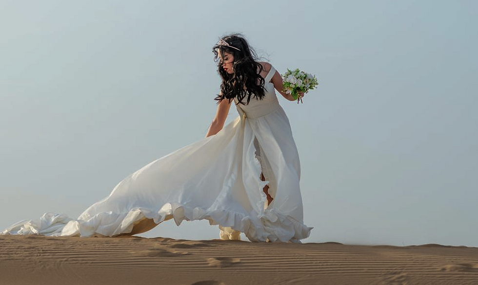 Bride in white dress holding bouquet on sand dunes