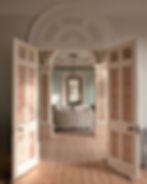 Open double doors lead to a living room with sofa and chandelier. Thelocationhouse