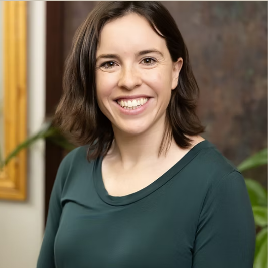 Smiling woman in green shirt, professional headshot, looks directly at camera.
