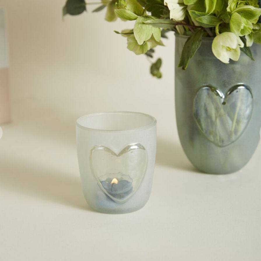 Frosted glass heart votive candle holder styled with greenery and ceramic vase on neutral tabletop