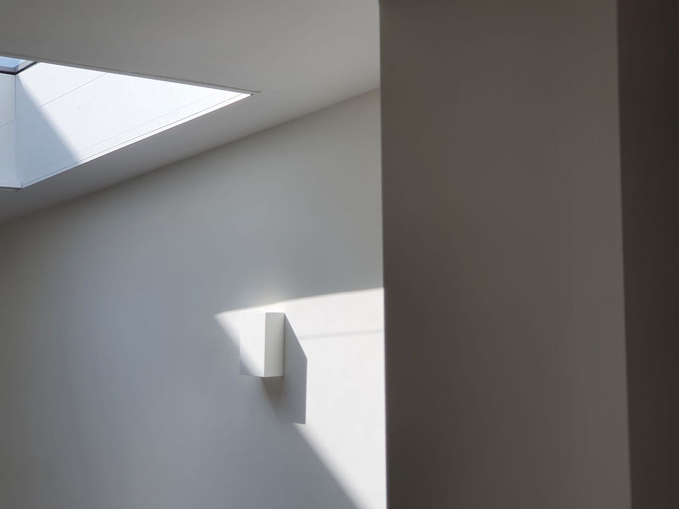 Minimalistic interior with a white wall, geometric shapes of light and shadow, and a conservation skylight above. Calm, quiet ambiance in North Norfolk.