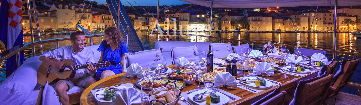 Aft dining area on Allure gulet with wooden table and cushions
