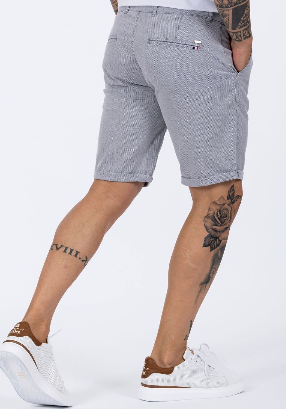 Homem a usar calções chino cinza claro slim fit com sapatilhas brancas em fundo branco