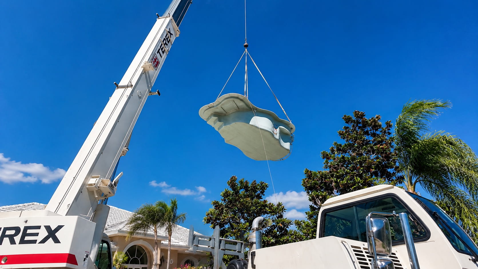 Crane lowering a fiberglass pool shell into a Florida backyard