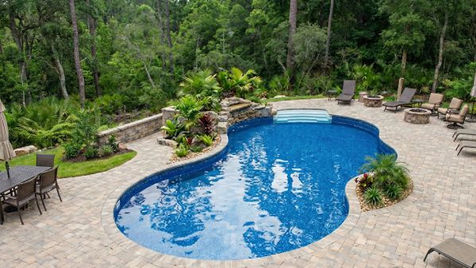 Custom-shaped backyard swimming pool with waterfall, paver patio, lush landscaping