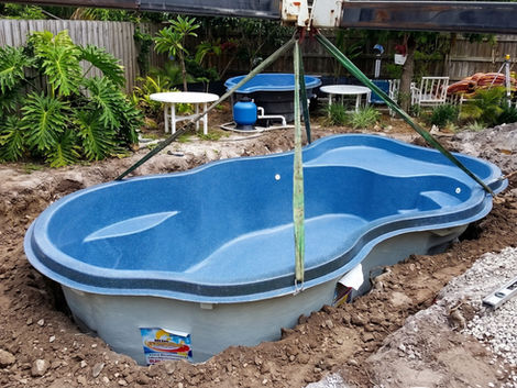 Blue fiberglass pool lowered into backyard excavation.