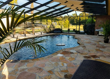 Screened swimming pool with flagstone patio and lush outdoor landscape.