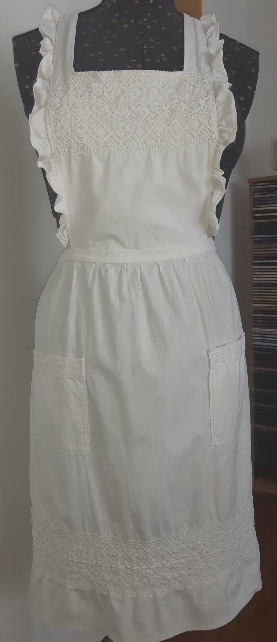 White vintage apron with frills and white braiding modelled on a dressmaker's doll