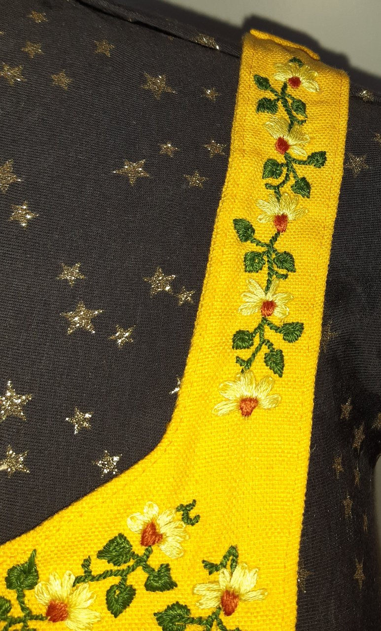 Close up view of embroidery of daisy flowers, stems and leaves on yellow apron
