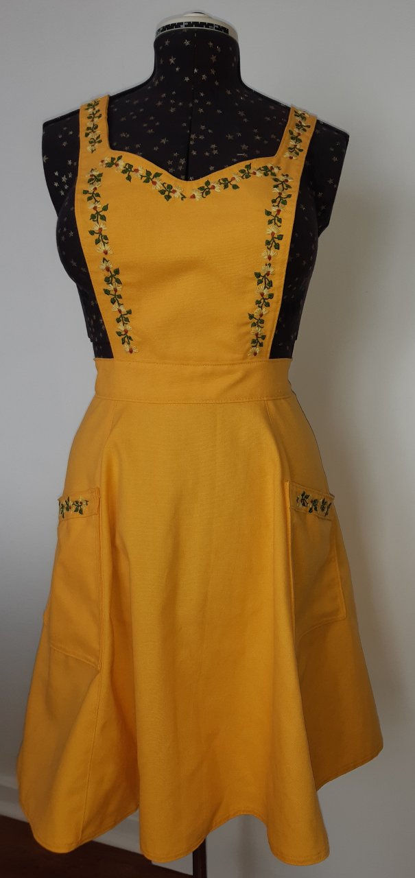 Yellow apron with full skirt and floral embroidery around the neckline, modelled on dressmaker's doll.