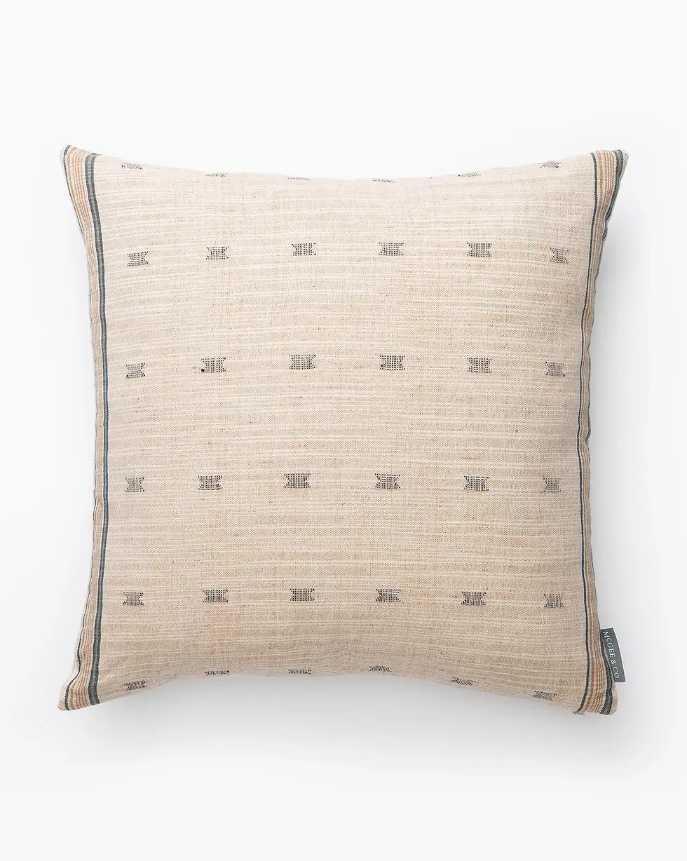 Beige pillow with subtle gray and black patterns set on a white background. Features thin gray borders and a small tag on the side.