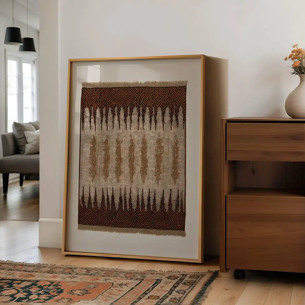 Framed textile art with geometric patterns leans against a wall. Nearby is a wooden cabinet with a vase. A cozy room with neutral tones.