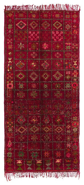 Red woven tapestry with intricate geometric patterns in green and yellow. Fringed edges, detailed motifs throughout, creating a rich, traditional look.