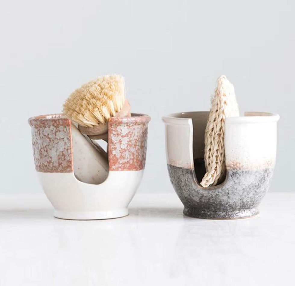 Two ceramic holders on a white surface, one with a brush, the other with a cloth. The left is reddish-brown, the right is gray. Minimalist feel.