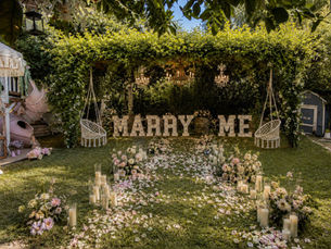 Illuminated MARRY ME garden proposal with a rose-petal path and two hanging swings at Le Petit Chateau du Jardin