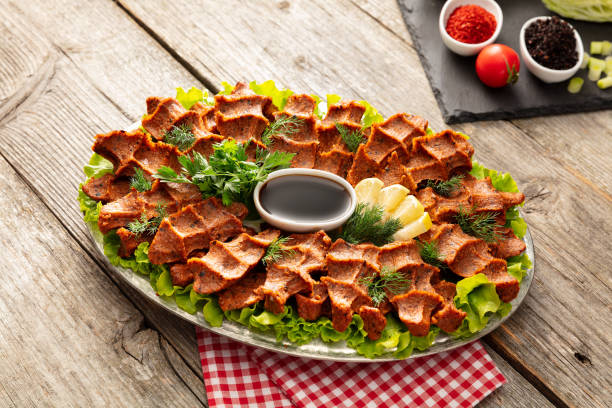 Bir tabakta marul yaprakları üzerinde çiğ köfte sunumu. Yanında limon dilimleri ve yeşillik. Tahta masa ve kareli örtü arka planda.