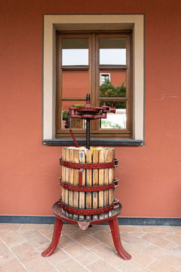 Vecchio torchio per vino in legno sotto finestra su muro rosso.