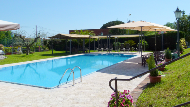 Grande piscina esterna con acqua cristallina, ombrelloni, lettini e prato verde.