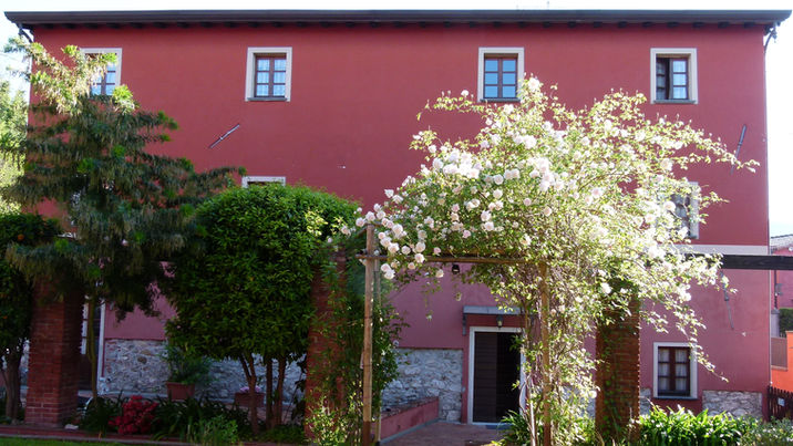 Grande edificio rosso con finestre, alberi verdi e arco fiorito.