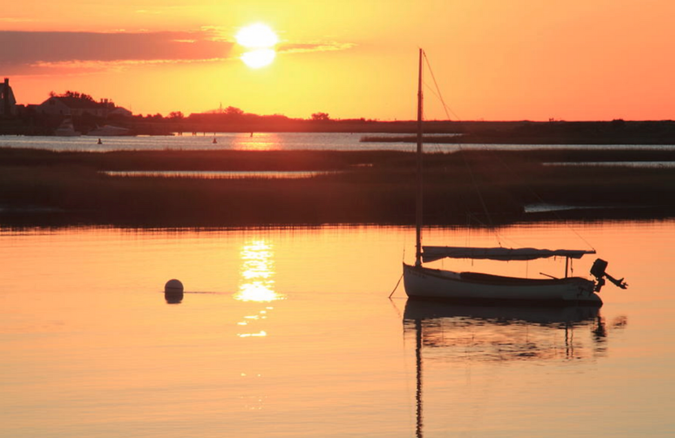 Small sailboat anchored in calm water at sunset.