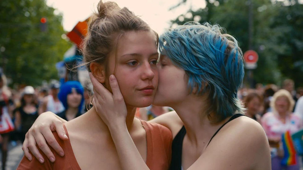 Escena de La Vie d'Adèle (2013), dir. Abdellatif Kechiche. Una mujer blanca de cabello azul sostiene el rostro de otra mujer blanca y la besa mientras ella sonríe.