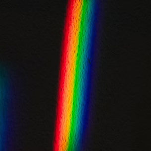 A imagen tiene un fondo negro, sobre el cual aparecen tres formas verticales luminosas, semejantes a franjas o reflejos de arcoíris desenfocados.