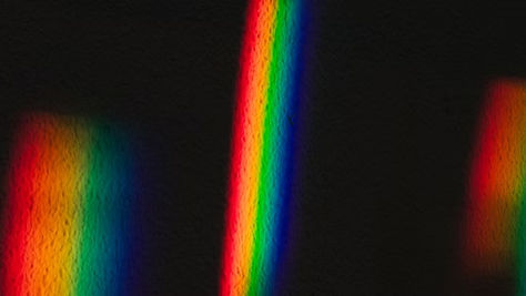 A imagen tiene un fondo negro, sobre el cual aparecen tres formas verticales luminosas, semejantes a franjas o reflejos de arcoíris desenfocados.