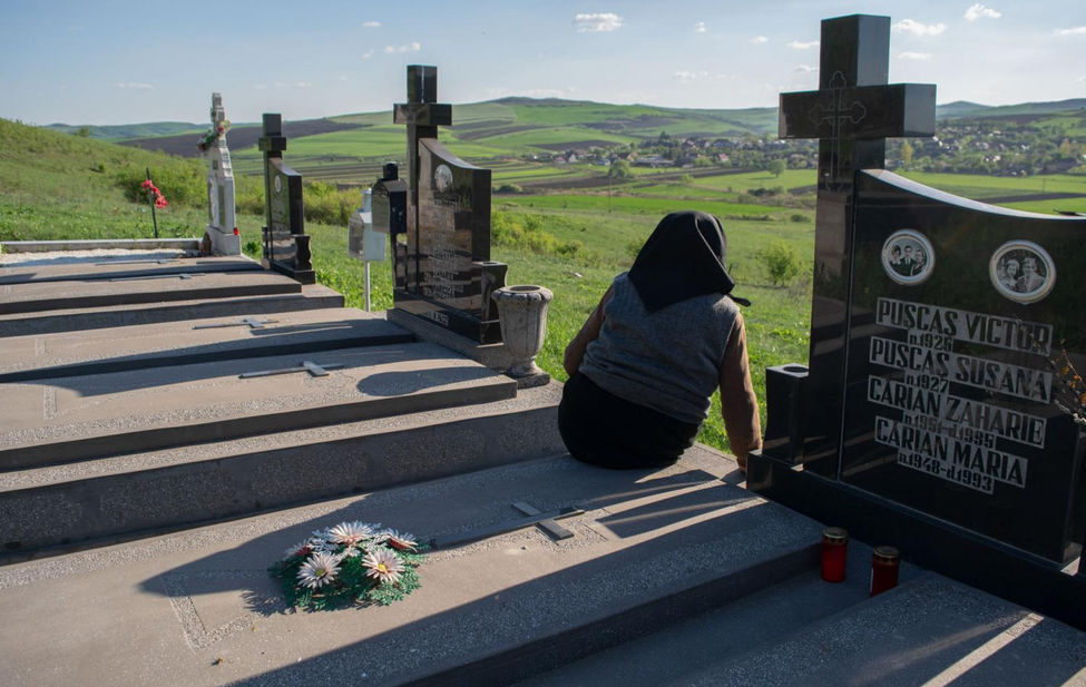 Documentary photograph of an elderly woman sitting by her husbands grave in Romania.