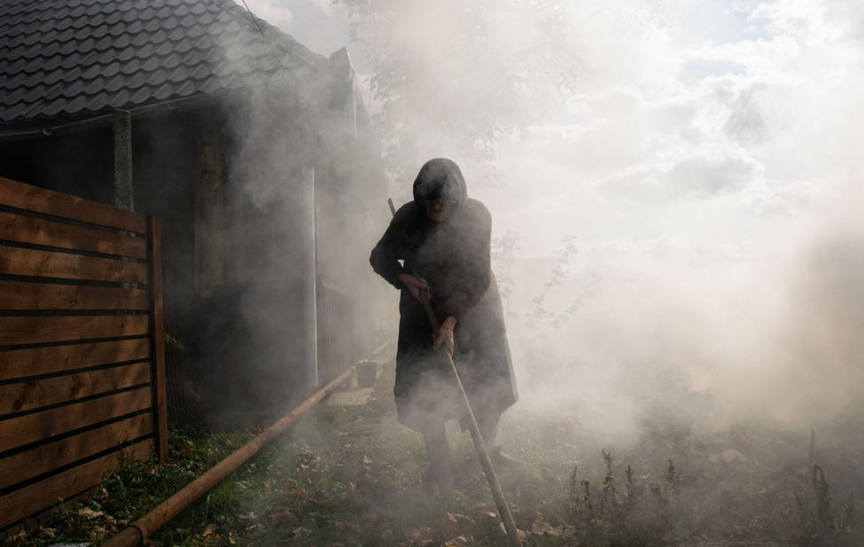 Documentary photograph of an elderly woman burning waste in Romania.