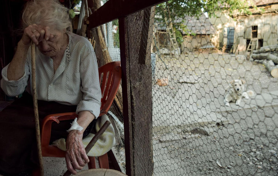 Documentary photograph of an elderly Romanian woman resting her head on a walking stick.