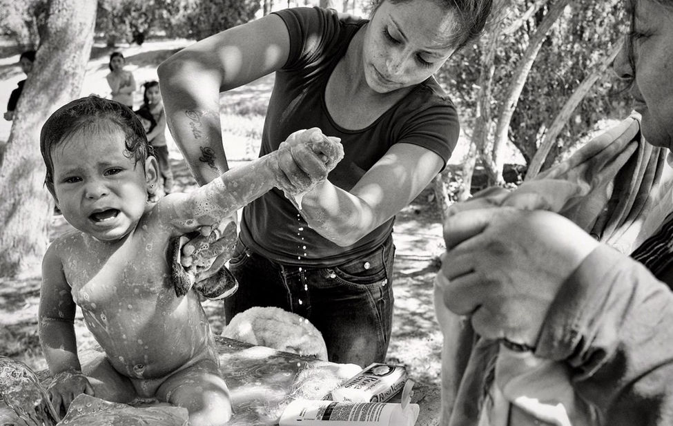 Documentary photograph of a migrant mother bathing her child.