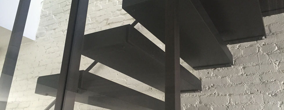 Close up view of floating wood treads with black metal railing and supports with glass partition