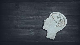 A cutout of a human head with cog wheels on black wood background