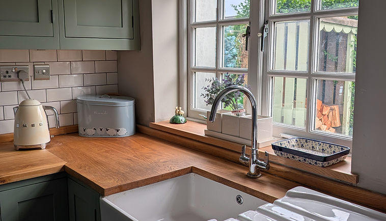 Refined traditional kitchen with painted shaker cabinetry, oak worktops, Belfast sink, timber window surround and handcrafted finishes by Bespoke Spray Studio.
