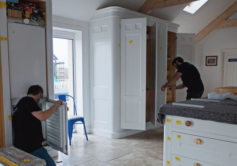 Kitchen cabinet doors being carefully removed by technicians during refinishing process in a residential kitchen