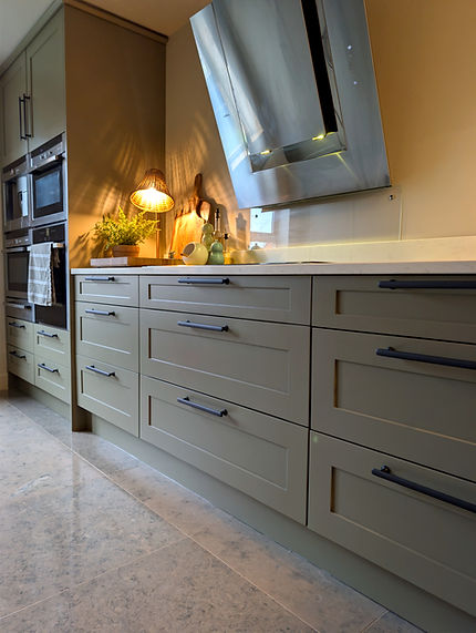 After photograph of the same Shaker kitchen drawers, refinished in muted grey-green Treron with new bronze drawer pulls. The existing worktops, hob and extractor have been retained.