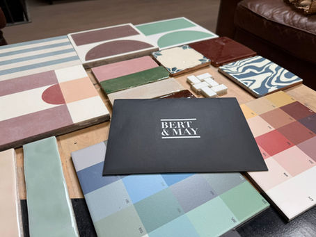 Selection of handmade tile samples and colour swatches from Bert & May displayed on a workshop table, including patterned tiles, pastel tones, and a sample folder.