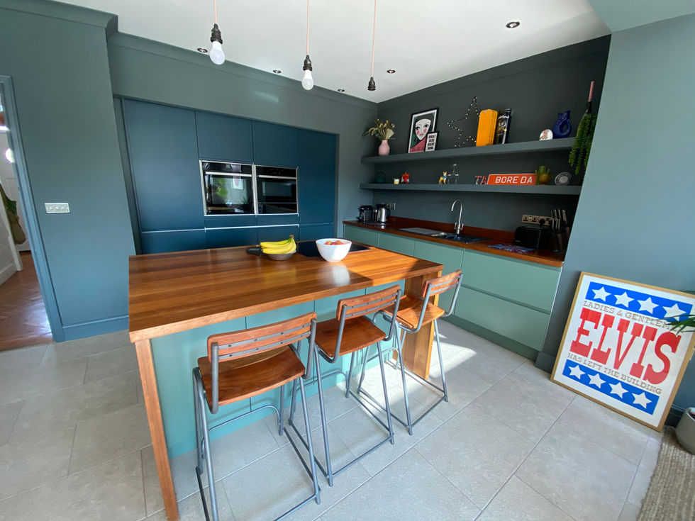 Contemporary kitchen resprayed in sage green and navy blue with open shelving, wooden stools, and a retro “Elvis” print for personality.