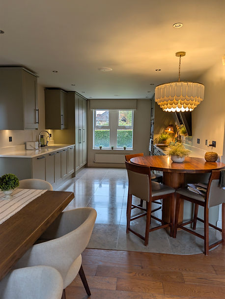 Completed kitchen refinement in Heath, Cardiff, with muted Treron Shaker cabinetry, Corston bronze hardware, pale stone flooring, a circular wooden dining table and a large scalloped pendant light.