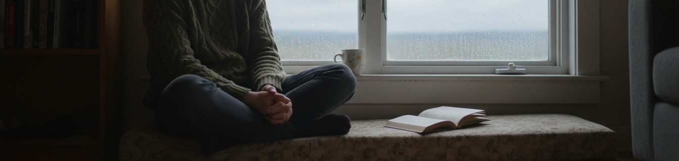 Eye-level view of a person sitting alone by a window on a cloudy morning