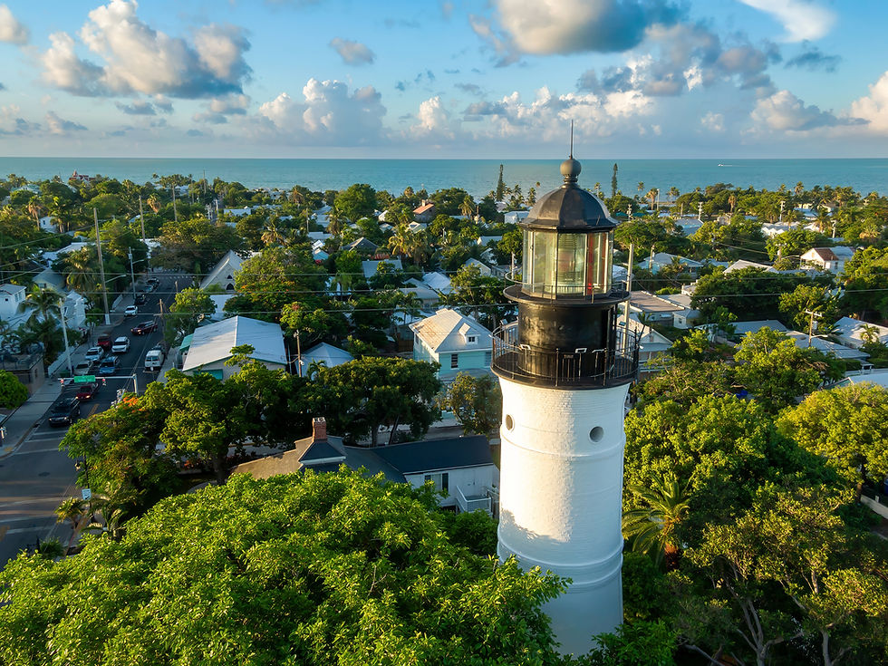 The Key West Lighthouse rising above the rooftops and tree canopy of Old Town Key West, with the ocean beyond