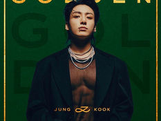 BTS member Jungkook poses in front of visuals from his solo exhibition “GOLDEN: The Moments,” which is set to open at Mehboob Studios in Mumbai, showcasing his artistry, performances, and creative journey.