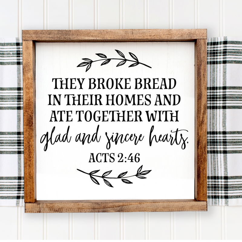 Wooden Scripture sign reading they broke bread in their homes and ate together with glad and sincere hearts, displayed in a d