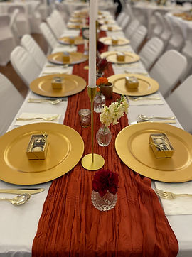 Chocolate truffle wedding favors on a set banquet table with gold chargers, a red table runner, and taper candles
