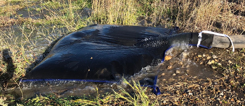 Heavy-duty dewatering bag with discharge hose inserted, laid out on a gravel construction site, filtering water while retaining sediment.
