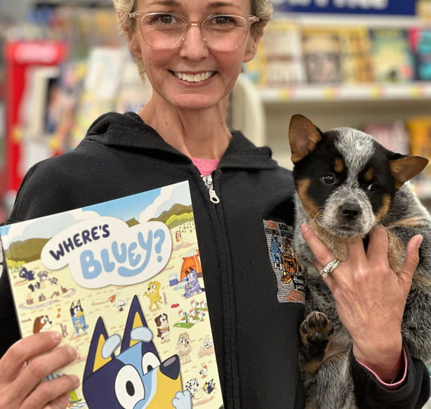 7 week old Bluey puppy held by a lady holding a bluey coloring book in walmart