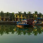 Palm trees and squat buildings dot the riverside, with two riverboats in the foreground
