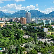 Tirana, a city with a colorful mix of pastel architecture, a lush park in the foreground, and the Dajti mountains in the background
