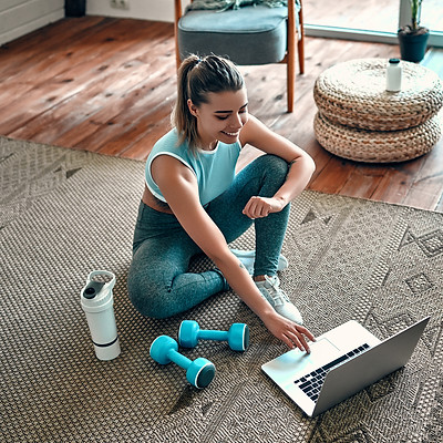 A sporty woman in sportswear is sitting on the floor with dumbbells and a protein shake or