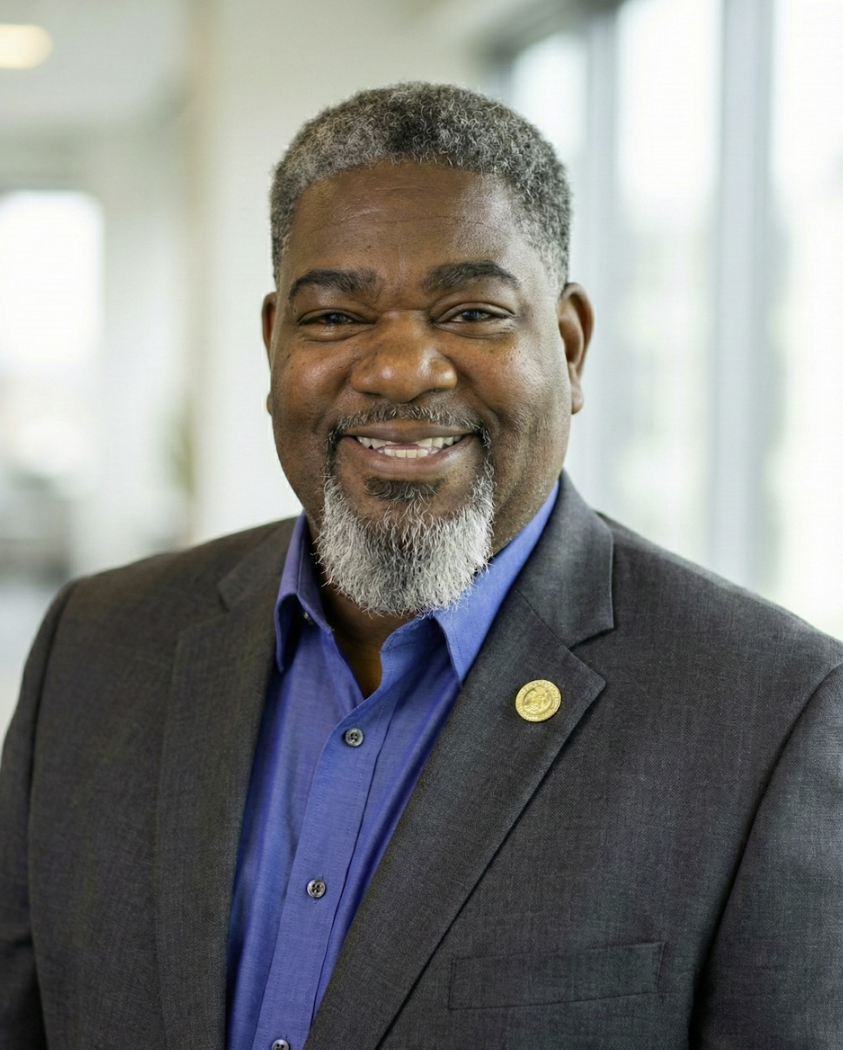This image shows Rawleigh Richardson Sr., a confident and approachable professional. He is an African American man with short gray hair and a neatly groomed beard, wearing a dark gray suit jacket over a blue dress shirt. His warm smile and poised demeanor convey leadership, trust, and professionalism — ideal for representing his role as Founder & Principal Consultant of HumanKind Consulting L.L.C.